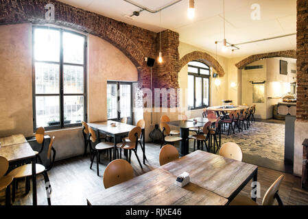 Tavoli e sedie di legno in un vuoto di ristorante rustico con grandi finestre ad arco e molta luce del sole Foto Stock