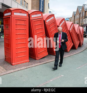 Un uomo controlla il telefono cellulare mentre si cammina passato caduti la casella Telefono installazione, 'out-of-order" da David Mach in Kingston-upon Thames. Foto Stock