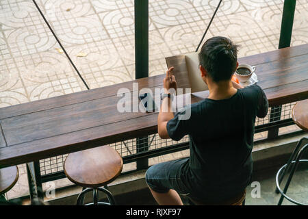 Uomo asiatico la lettura di libri e di bere il caffè al mattino Foto Stock