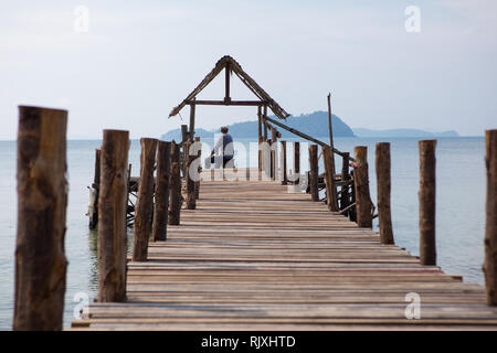 Il vecchio uomo si siede sul molo e guarda al mare Foto Stock