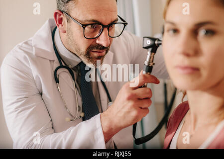 Il medico ORL controllo orecchio con otoscopio di donna paziente in ospedale. Esame medico orecchio del paziente femmina con uno strumento. Foto Stock