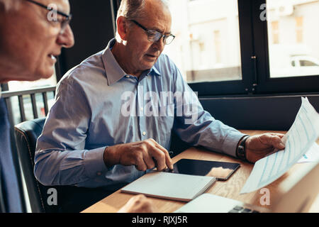 Imprenditore senior con il collega di lavoro su una relazione di affari. Due partner commerciali analizzando alcuni documenti mentre si è seduti al cafe tramite digital tabl Foto Stock