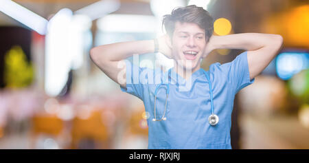 Giovane medico medico che indossano uniformi su sfondo isolato rilassante e stretching con le braccia e le mani dietro la testa ed il collo, sorridendo felice Foto Stock