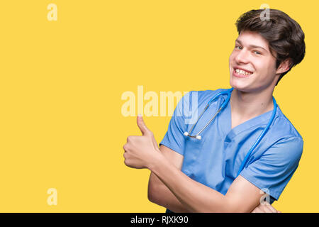 Giovane medico medico che indossano uniformi su sfondo isolato cercando orgogliosi, sorridente facendo pollice fino al gesto del lato Foto Stock