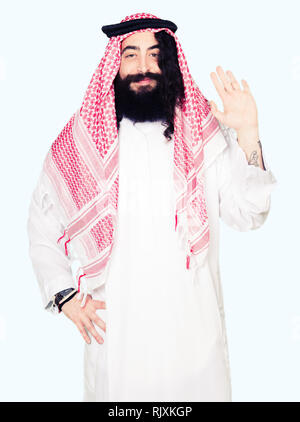 Arabian business man con capelli lunghi indossando il tradizionale keffiyeh sciarpa rinuncia a dire ciao felice e sorridente, gentile gesto di benvenuto Foto Stock