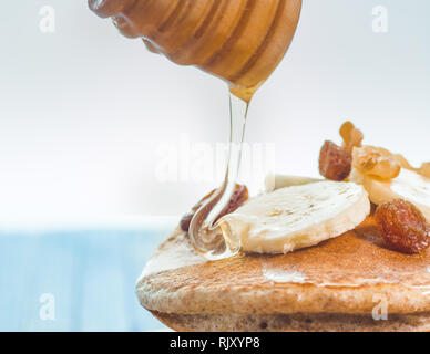 Close up di far cadere il miele sul grano intero pancake con banane fresche ,uva passa e noci, miele . sana colazione con frutta e noci Foto Stock