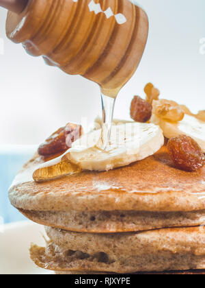 Close up di far cadere il miele sul grano intero pancake con banane fresche ,uva passa e noci, miele . sana colazione con frutta e noci Foto Stock