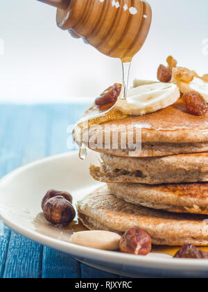 Close up di far cadere il miele sul grano intero pancake con banane fresche ,uva passa e noci, miele . sana colazione con frutta e noci Foto Stock