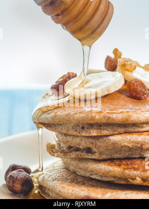 Close up di far cadere il miele sul grano intero pancake con banane fresche ,uva passa e noci, miele . sana colazione con frutta e noci Foto Stock