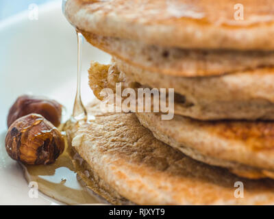 Close up di far cadere il miele sul grano intero pancake con banane fresche ,uva passa e noci, miele . sana colazione con frutta e noci Foto Stock