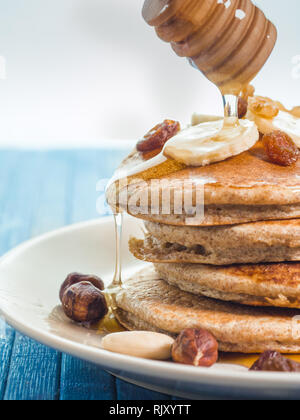 Close up di far cadere il miele sul grano intero pancake con banane fresche ,uva passa e noci, miele . sana colazione con frutta e noci Foto Stock