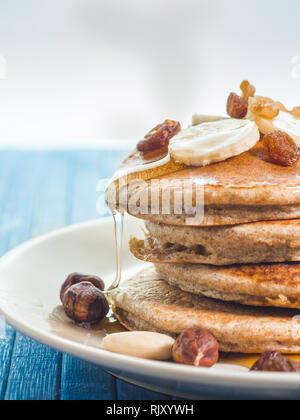 Close up di far cadere il miele sul grano intero pancake con banane fresche ,uva passa e noci, miele . sana colazione con frutta e noci Foto Stock