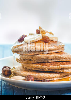 La caduta del miele per tutto il frumento pancake con banane fresche ,uva passa e noci, miele . sana colazione con frutta e noci Foto Stock