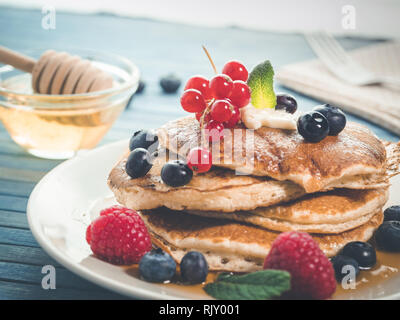 Close up di pancake con mirtilli freschi , lamponi e ribes rosso, originale american pancake con miele, dolce colazione. sana colazione w Foto Stock
