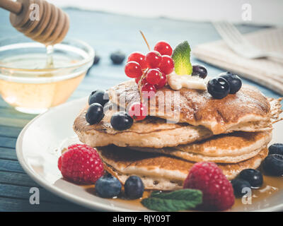 La caduta del miele per pancake con mirtilli freschi , lamponi e ribes rosso, originale american pancake con miele, dolce colazione. break sani Foto Stock