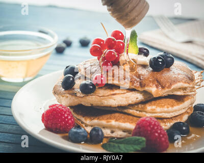 La caduta del miele per pancake con mirtilli freschi , lamponi e ribes rosso, originale american pancake con miele, dolce colazione. break sani Foto Stock