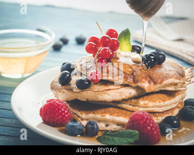 La caduta del miele per pancake con mirtilli freschi , lamponi e ribes rosso, originale american pancake con miele, dolce colazione. break sani Foto Stock