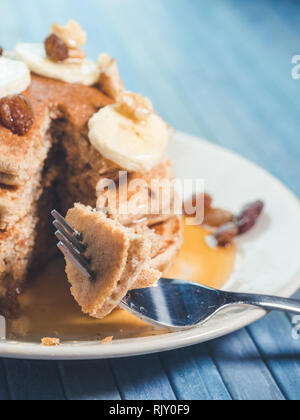 Mangiare con il fork di un grano intero pancake con banane fresche ,uva passa e noci, miele . sana colazione con frutta e noci Foto Stock