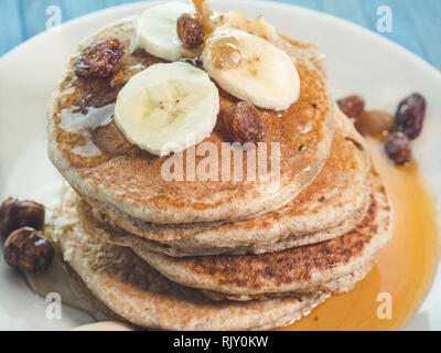 Vista superiore del miele di caduta su tutto il frumento pancake con banane fresche ,uva passa e noci, miele . sana colazione con frutta e noci Foto Stock