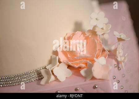 Close up di glassa delicate decorazioni floreali su una torta a più livelli, abbellito con velluto rosa pastello ciliegina, fiori di zucchero e argento gioielli commestibili Foto Stock