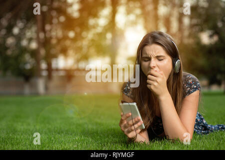 Ragazza sbadigliare annoiato con il contenuto in linea in possesso di un telefono cellulare Foto Stock