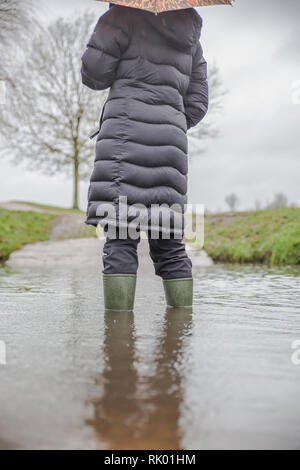 Kidderminster, Regno Unito. 8 febbraio 2019. Regno Unito tempo: Pioggia pesante persistente conduce ai livelli di acqua che aumentano nel Worcestershire con le acquazzoni blustery che continuano durante il giorno. Una giovane donna, vista posteriore, indossando lungo, cappotto invernale e wellies è in piedi isolato all'aperto in acqua alluvione invernale. Credit: Lee Hudson/Alamy Live News Foto Stock