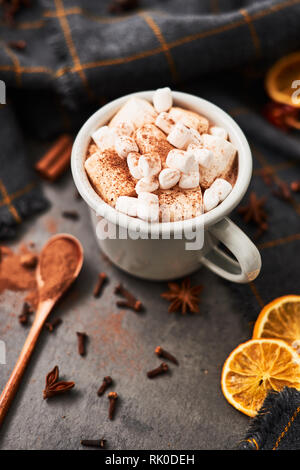 Cioccolata calda bevanda con marshmallows rétro mug circondato da ingredienti: cannella, arancio, anice e cove sul calcestruzzo nero tabella. Inverno bere. Parte superiore Foto Stock