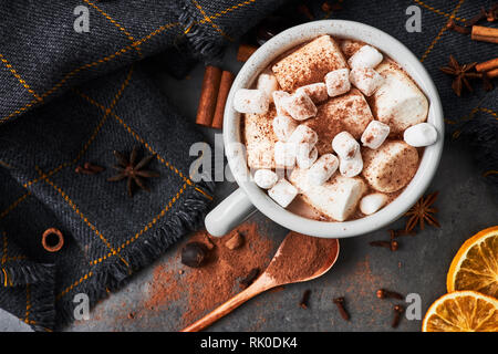 Cioccolata calda bevanda con marshmallows rétro mug circondato da ingredienti: cannella, arancio, anice e cove sul calcestruzzo nero tabella. Inverno bere. La formazione di ruggine Foto Stock