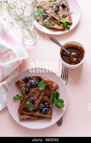 Cioccolato artigianale crepes servita con mirtilli, il sugo di pomodoro e le foglie di menta su sfondo rosa. Messa a fuoco selettiva. Vista dall'alto. Spazio di copia Foto Stock