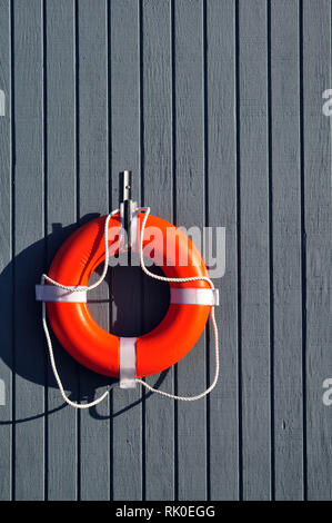 Un arancio salvagente appeso ad un muro grigio di una boathouse Foto Stock