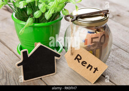 Pagamento del noleggio concetto - denaro jar, chiave con etichetta e piccola casa sulla scrivania in legno Foto Stock