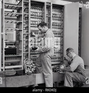 Degli anni Cinquanta, maschio tecnici che lavorano in una fabbrica di aviazione le tensioni di prova con mano voltmetri analogici o lettori di metro. Foto Stock