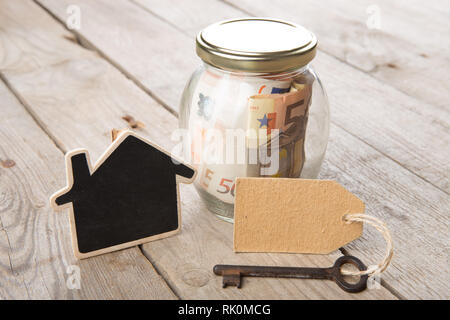 Finanza immobiliare concetto - denaro di vetro con chiave vintage e piccola casa Foto Stock