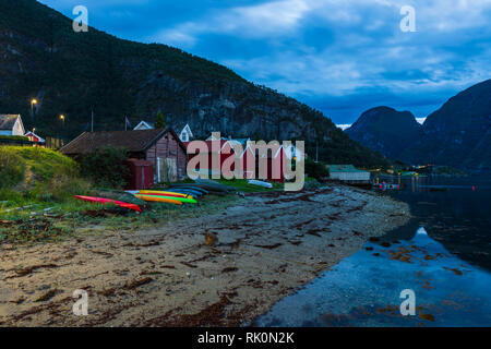 Fila di capovolto vivacemente colorato canoe da capanne in legno e riverbank, distante shot, Aurland, Norvegia, Europa Foto Stock