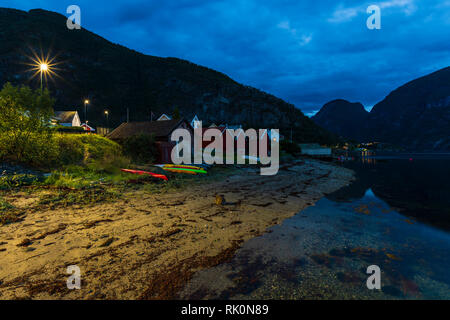 Fila di capovolto vivacemente colorato canoe da capanne in legno e riverbank, distante shot, Aurland, Norvegia, Europa Foto Stock