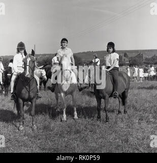 1964, ragazze su pony o piccoli cavalli in un campo di prendere parte ad un cavallo gymkhana, England, Regno Unito, equestre comprendente anche diverse gare a cavallo. Foto Stock