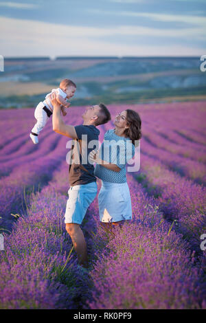 Ritratto di famiglia madre padre e figlio bambino sul campo di lavanda per divertirsi insieme. Coppia felice con bambino godetevi una vacanza semplice da indossare jeans blu clo Foto Stock