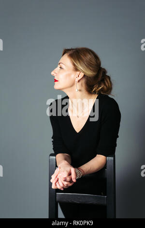 Ritratto di donna bella in un abito nero contro lo sfondo grigio Foto Stock