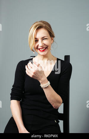 Ritratto di donna bella in un abito nero contro lo sfondo grigio Foto Stock