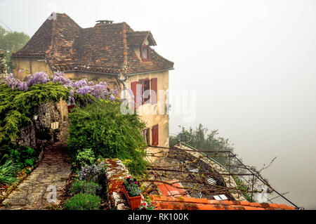 Secoli vecchia casa di pietra si siede nella nebbia a bordo della scogliera che si affaccia sul fiume Lot nella parte sud-ovest della Francia città medievale di San Cirque Lapopie. Foto Stock