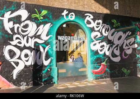 Donne al ristorante Wagamama con From Your Bowl to Borough's Soul dipinte su una parete esterna a Southwark, Bankside, Londra, Regno Unito a febbraio Foto Stock