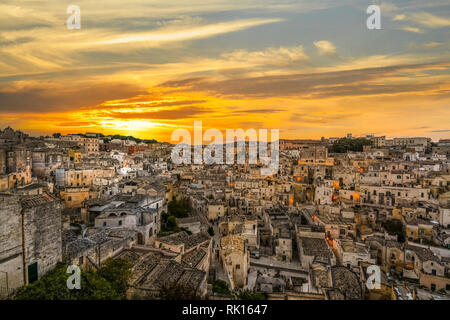 Un Dorato, colorato tramonto sopra l'antica città di Matera in Italia, come le luci si accendono e si illuminano le chiese, torri, edifici abbandonati. Foto Stock