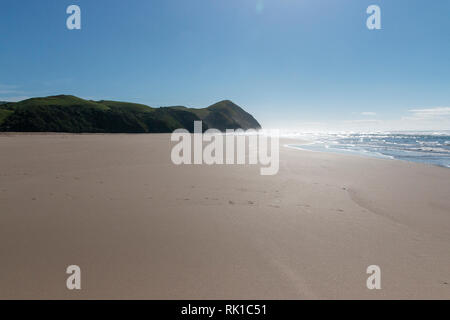 Una spiaggia vuota dove la sabbia conduce fino a una montagna e l'acqua oceanica in background Foto Stock