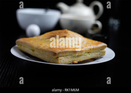 Bollitore per tè e pasticcini - piastra bianca con una torta e una teiera e tazzina in background Foto Stock