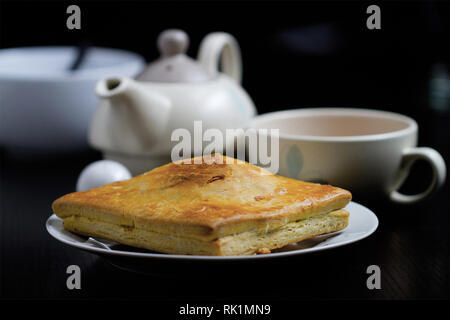 Bollitore per tè e pasticcini - piastra bianca con una torta e una teiera e tazzina in background Foto Stock