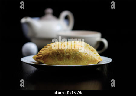 Bollitore per tè e pasticcini - piastra bianca con torte e una teiera e tazzina in background Foto Stock