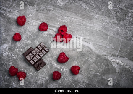 Fresche lamponi organici e due barre di organico 70% di cacao al cioccolato fondente su una pietra di marmo con uno sfondo con spazio di copia Foto Stock