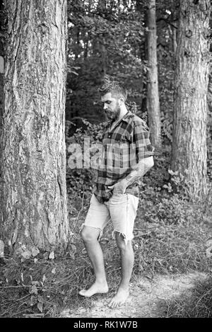 Uomo Barbuto nella foresta. Hipster con lunga barba di verde naturale paesaggio. Tourist in plaid shirt e Jean Corti il viaggio a piedi nudi. Traveler escursionismo su Foto Stock