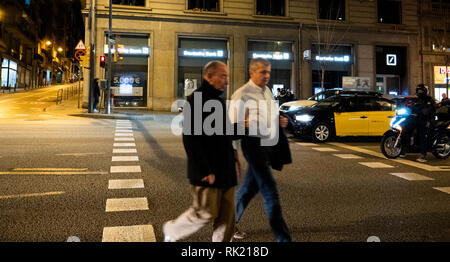 Barcellona, Spagna - Nov 11, 2017: Senior uomini attraversamento strada di notte sulla Via Augusta viale nel centro di Barcellona con la Deutsche Bank office in background Foto Stock