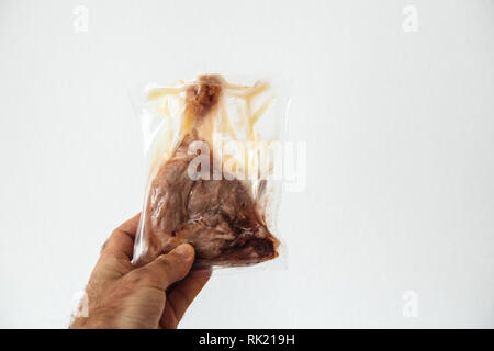 Man mano che tiene in mano contro uno sfondo bianco di una gamba di anatra conservato in un sacchetto di plastica Foto Stock